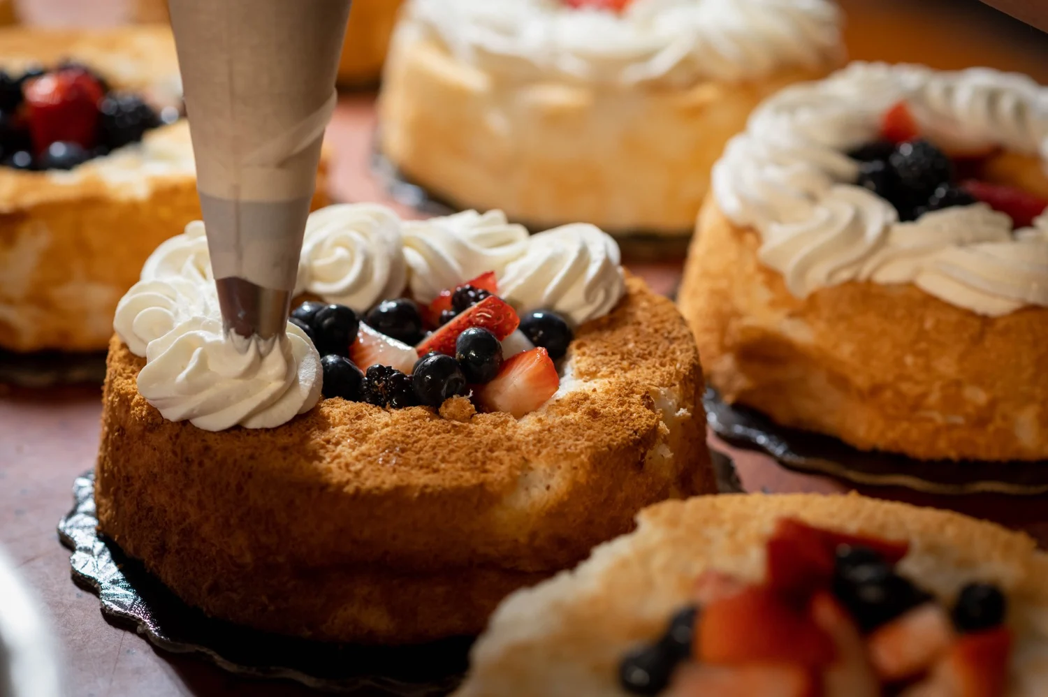 Fresh angel food cakes being finished with cream and berries